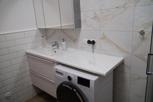 a white bathroom with a washing machine under a sink at Apartament Ostoya 2 w centrum Ełku in Ełk