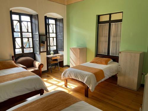 a bedroom with two beds and a chair and windows at Villa Bonita Hostel in Riobamba