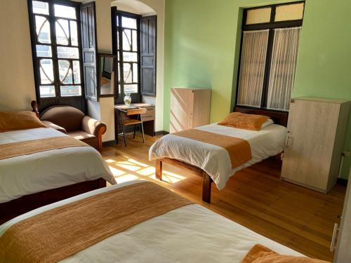 Habitación con 2 camas, silla y ventanas. en Villa Bonita Hostel en Riobamba