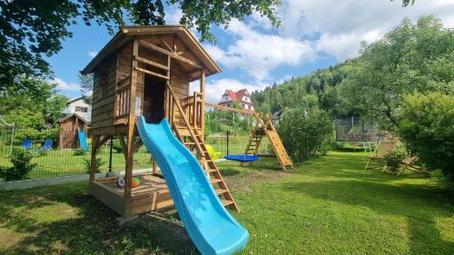 een speeltuin met een glijbaan en een speelhuis bij Korona Pienin Domki & Apartamenty in Szczawnica