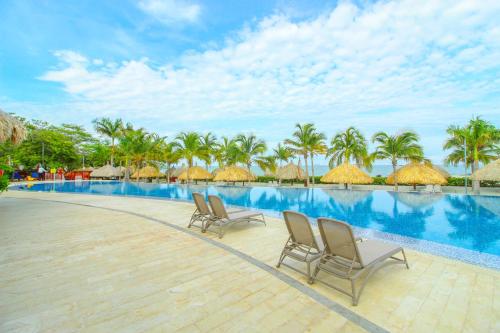 a resort swimming pool with two chairs and palm trees at Apartasuites Samaria - Club de Playa in Santa Marta