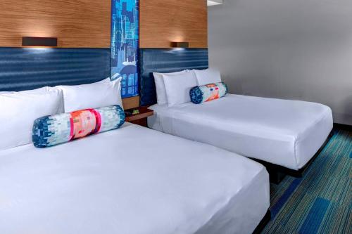 2 camas en una habitación de hotel con sábanas y almohadas blancas en Aloft Raleigh Durham Airport Brier Creek, en Raleigh