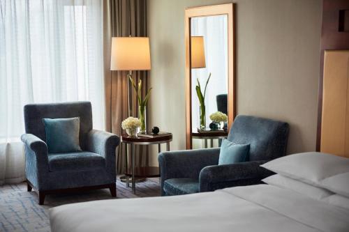 um quarto de hotel com duas cadeiras e uma cama e um espelho em Renaissance Wuhan Hotel em Wuhan