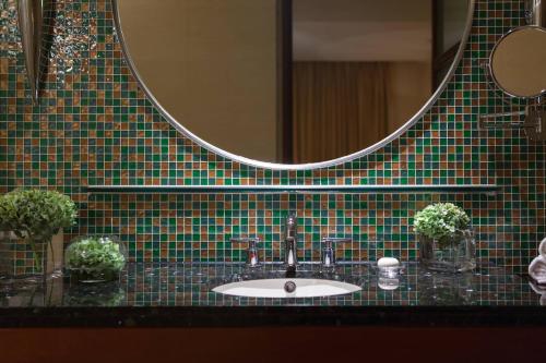 lavabo en el baño con pared de azulejos verdes y espejo en Renaissance Wuhan Hotel, en Wuhan