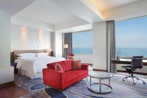 um quarto de hotel com uma cama, uma cadeira vermelha e uma secretária em Four Points by Sheraton Manado em Manado