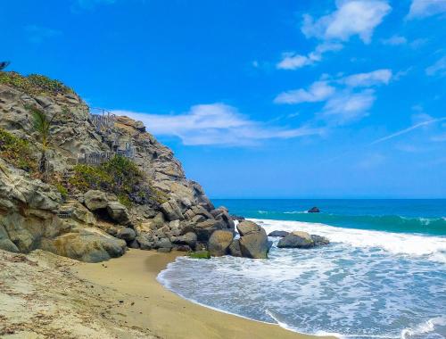 a beach with rocks and the ocean on a sunny day at Hotel Casa Barlovento, Parque Tayrona in Los Naranjos
