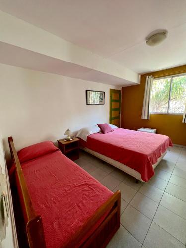 a bedroom with two beds with red sheets and a window at Hotel Village Termas de Dayman in Termas del Daymán