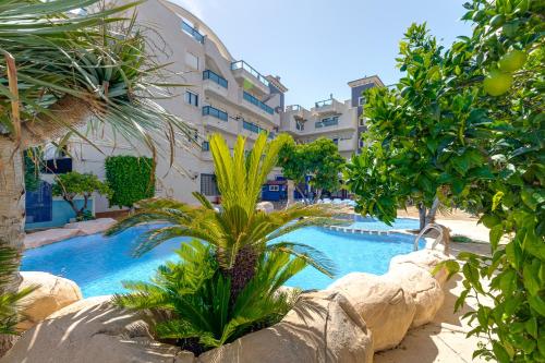 a swimming pool with a palm tree in front of a building at Penthouse Naomi with two terraces, private solarium, sea view, swimming pool, with underground parking, pets allowed in Orihuela Costa