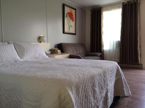 a bedroom with a white bed and a chair at Motel de la Pente Douce in Magog-Orford