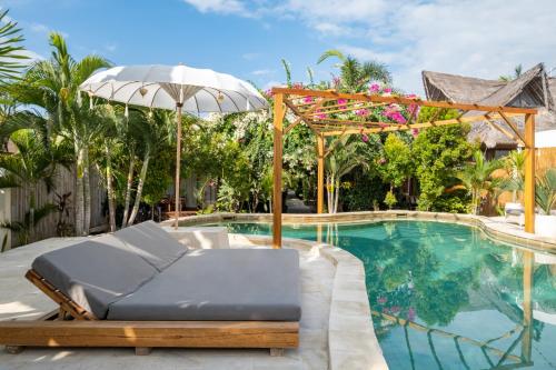 a bed with an umbrella next to a swimming pool at Gili Teak Beach Front Resort in Gili Trawangan
