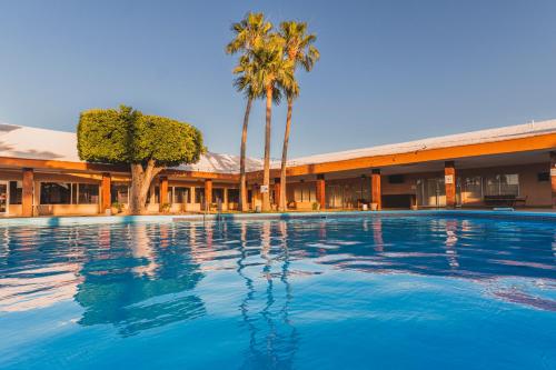 a swimming pool in front of a building with palm trees at El Camino Hotel & Suites in Heroica Caborca