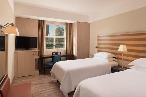 a hotel room with two beds and a desk and a television at Sheraton Rome Parco de Medici in Rome