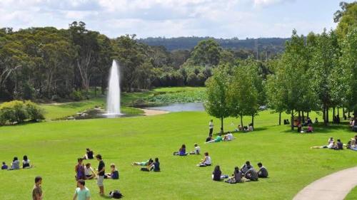 people sitting in the grass in a park with a fountain at Private Bath Ensuite Room Eastwood/MQ Uni park in Sydney