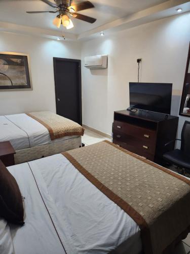 a bedroom with two beds and a dresser and a tv at Hotel Don Quijote in Mexicali
