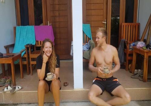 un hombre y una mujer sentados en los escalones con tazas de café en Merendeng Hostel Kuta, en Kuta Lombok