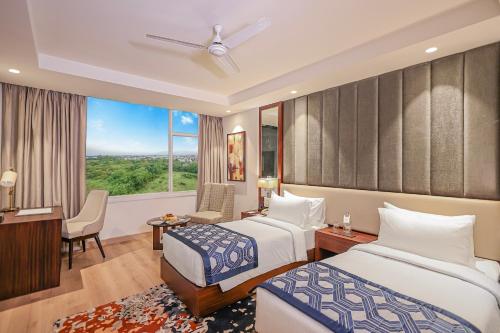 a hotel room with two beds and a desk and a window at Regenta Dehradun by Royal Orchid Hotels Limited in Dehradun