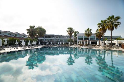 a large swimming pool with chairs and palm trees at Flora Garden BEACH - Couples Concept - Adults over 16 Only in Kızılot