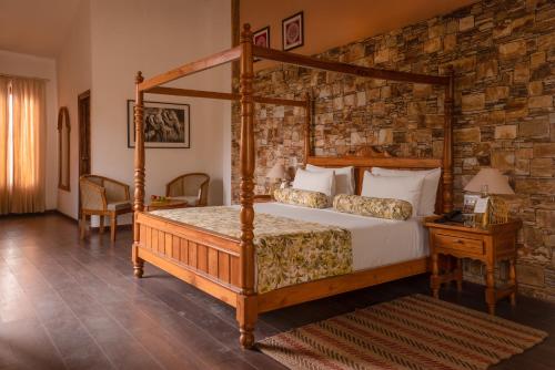 1 dormitorio con cama con dosel y pared de piedra en Tree of Life Vanvilas Riveredge Corbett en Rāmnagar