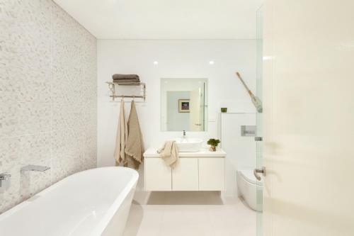 Baño blanco con bañera y lavamanos en Kiama Waterfront Apartment en Kiama