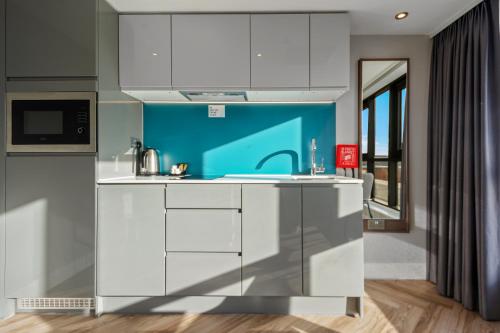 a kitchen with white cabinets and a blue wall at Roomzzz Newcastle City in Newcastle upon Tyne
