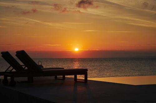 a sunset on the beach with two chairs and the ocean at Ducato di Zante Luxury Beach Villa, by ZanteWize in Kipseli