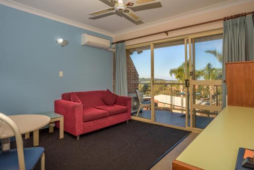 a living room with a red chair and a balcony at Sapphire Waters Motor Inn in Merimbula