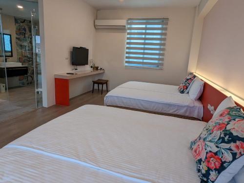 two beds in a room with a television and a bathroom at Agape Homestay in Magong