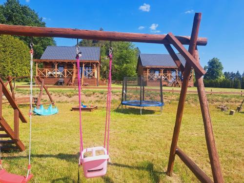 a playground with swings and a cabin in the background at Domki Na Wzgórzu - domek nr 2 in Mrągowo