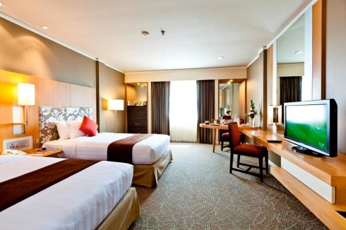 a hotel room with two beds and a desk with a television at Royal Princess Larn Luang - SHA Extra Plus in Bangkok