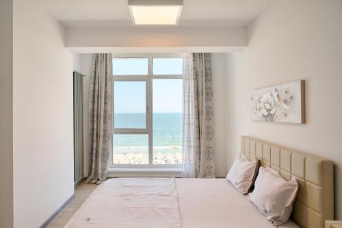 een slaapkamer met een raam met uitzicht op het strand bij Paradise Sea View 2BD apt Spa n Pools beach resort in Mamaia Nord – Năvodari