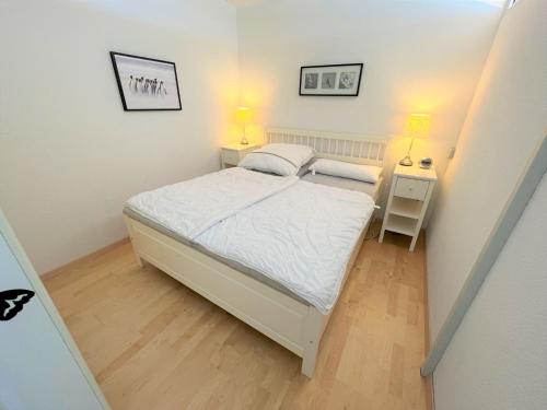 a small bedroom with a white bed and two lamps at Panoramic App A09-5 in Sierksdorf