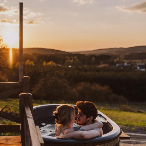a man and woman in a bath tub with the sunset at Jurty z widokiem, prywatna balia- DZIKOLAS GLAMPING in Krasnobród