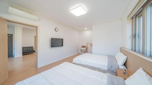 a bedroom with two beds and a tv on the wall at Maremonte Pension in Geoje 