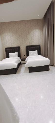 two beds in a bedroom with white floors and curtains at شاليهات أبيات الفندقية in Al Baha