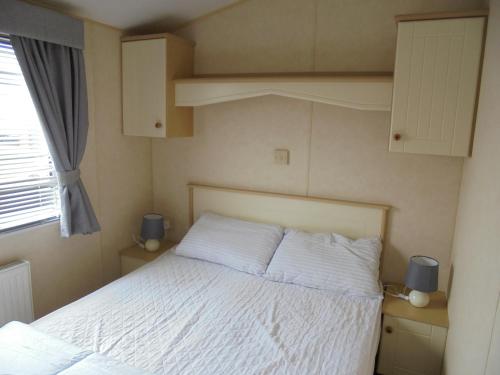 a bedroom with a bed with white sheets and a window at The Grange: Solstice:- 6 berth, enclosed veranda in Ingoldmells
