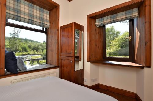 a bedroom with a bed and two windows at Cairnbaan House in Cairnbaan