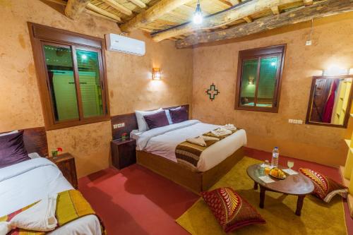 a bedroom with two beds and a table and windows at Palais Ksar Lamane in Aït Ben Haddou