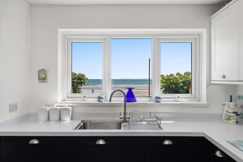eine Küche mit Spüle und zwei Fenster mit Meerblick in der Unterkunft Strand Cottage - Direct Beach Access in Saundersfoot
