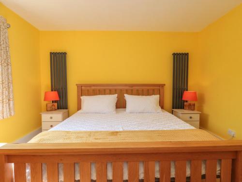 a bedroom with a bed with yellow walls and two lamps at Foxes Den in Ferndown