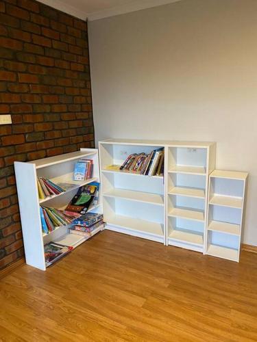 two white book shelves in a room with a brick wall at Comfortable Home in Camden Park in Plympton