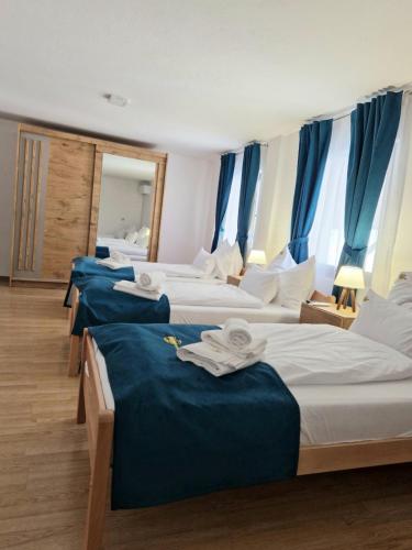 a row of four beds in a room with blue curtains at Apartmani Leburic in Prnjavor