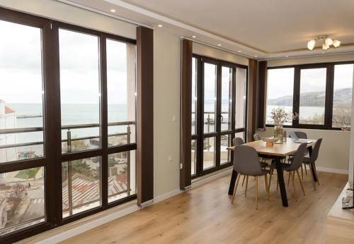 una sala da pranzo con tavolo, sedie e ampie finestre di Seaview Haven - Elegant 2BD Flat in Balchik by Flat Mаnager a Balchik