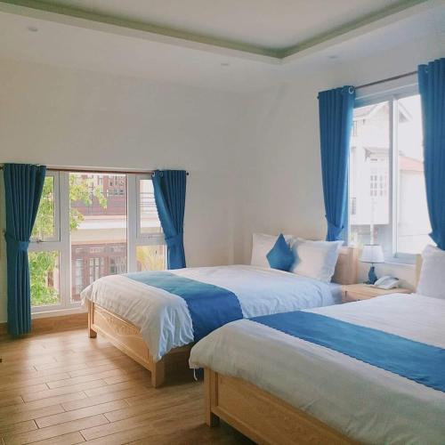 a bedroom with two beds with blue curtains and a window at The Light Hotel in Da Lat