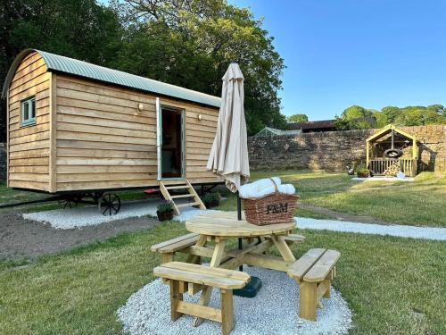 a picnic table and an umbrella next to a cabin at Secret Garden Shepherd Hut in Macclesfield