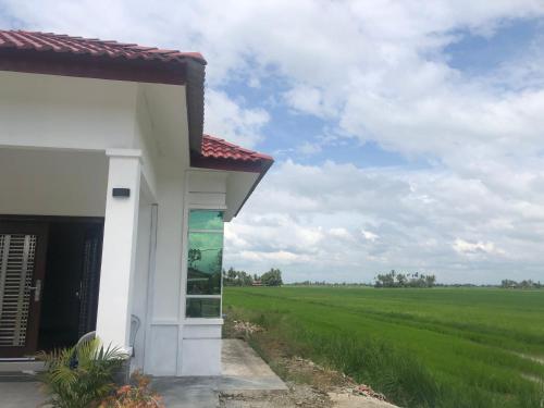 a white building with a field in the background at Aisyy homestay in Kampong Sungai Baru