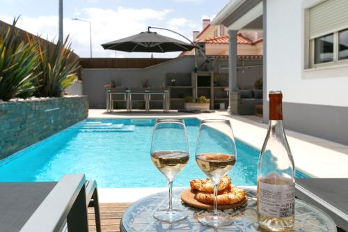 two glasses of wine on a table next to a swimming pool at Óbidos Pool & Charm in Óbidos