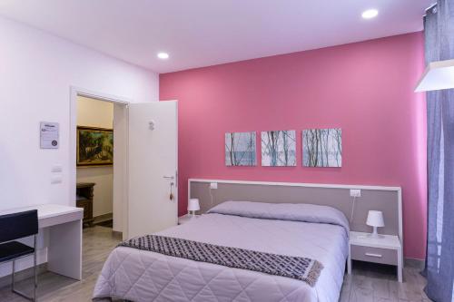 ノヴァーラにあるVentitrémarzo Guest Houseのピンクの壁のベッドルーム(ベッド1台、デスク付)