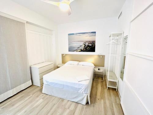 ein weißes Schlafzimmer mit einem Bett und einem Gemälde an der Wand in der Unterkunft Apartamentos Hotel Puente de Hierro in Benicàssim