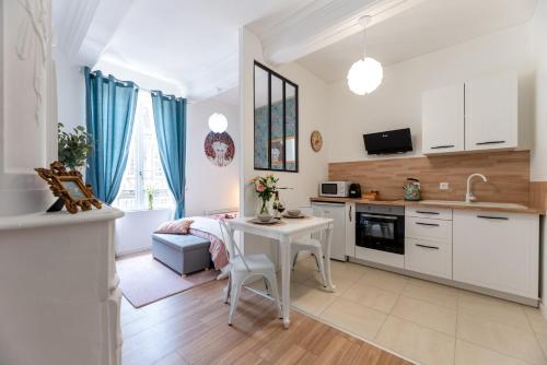 a kitchen with a white table and a kitchen with blue curtains at Pénélope by Kleidos - Charmant Studio Centre Pont-Audemer in Pont-Audemer