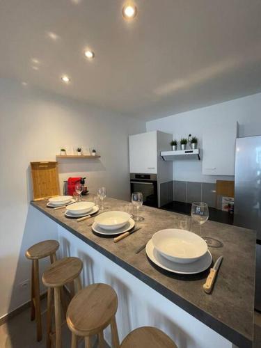 - une cuisine avec un comptoir avec des chaises, des assiettes et des verres à vin dans l'établissement Appartement T2 La Ferté Gaucher à 200m du centre, à La Ferté-Gaucher